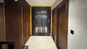A modern hallway with a marble floor, a wooden panel wall, and a yellow accent wall leading to an elevator. - Hotel Ganga Aamantran (Haridwar)