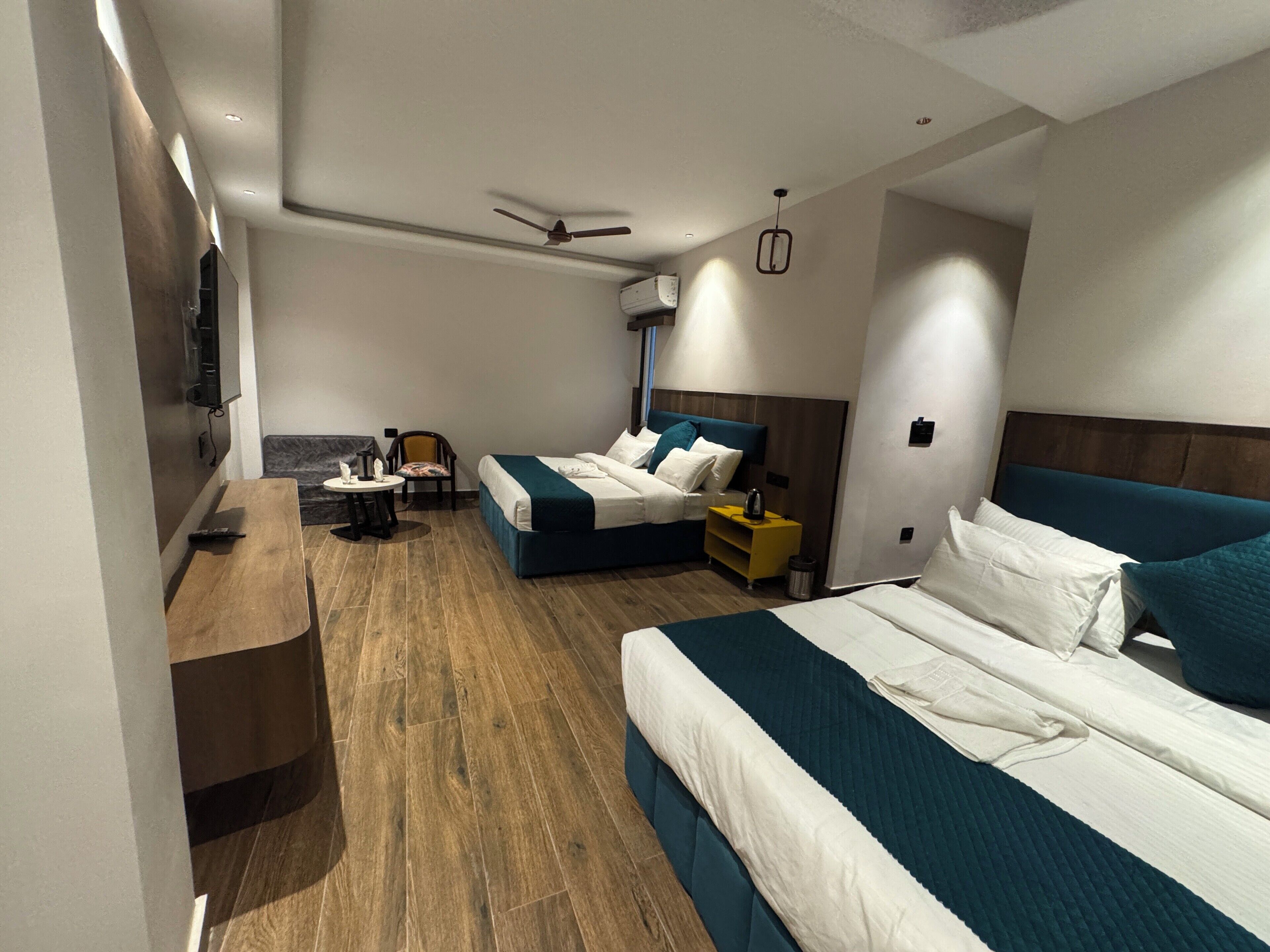 A modern hotel room with two beds, a desk, a chair, and a ceiling fan.