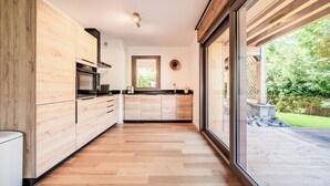 A modern kitchen with wooden cabinetry, a central island, and large windows offering a view of the outdoors.