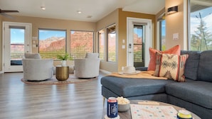 A spacious living room with a large gray sectional sofa, two armchairs, and a coffee table. The room features large windows with a view of red rock formations. - Mid-century Gem w/ Views, Hot Tub & Sunroom Lounge Red Rock Haven by Avantstay (Sedona)
