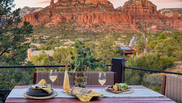 A dining table set with plates, glasses, and a bottle, overlooking a mountainous landscape. - Mid-century Gem w/ Views, Hot Tub & Sunroom Lounge Red Rock Haven by Avantstay (Sedona)