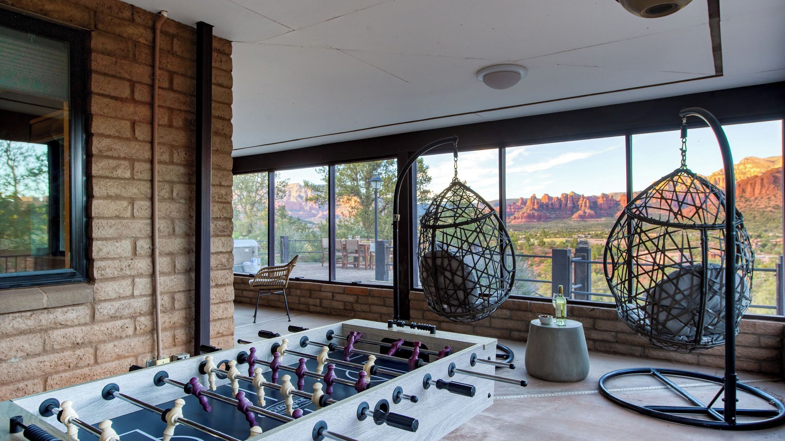 Una habitación con mesa de futbolín, sillas colgantes y vistas a formaciones rocosas rojas.