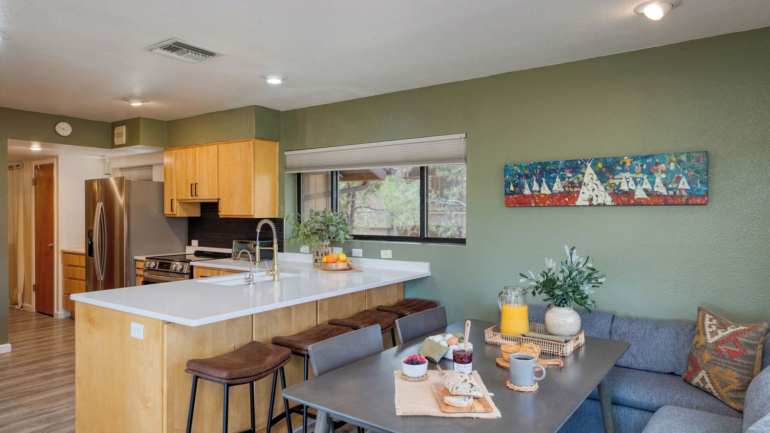 A modern kitchen with wooden cabinets, a stainless steel refrigerator, and a dining area with a gray table and blue sofa.