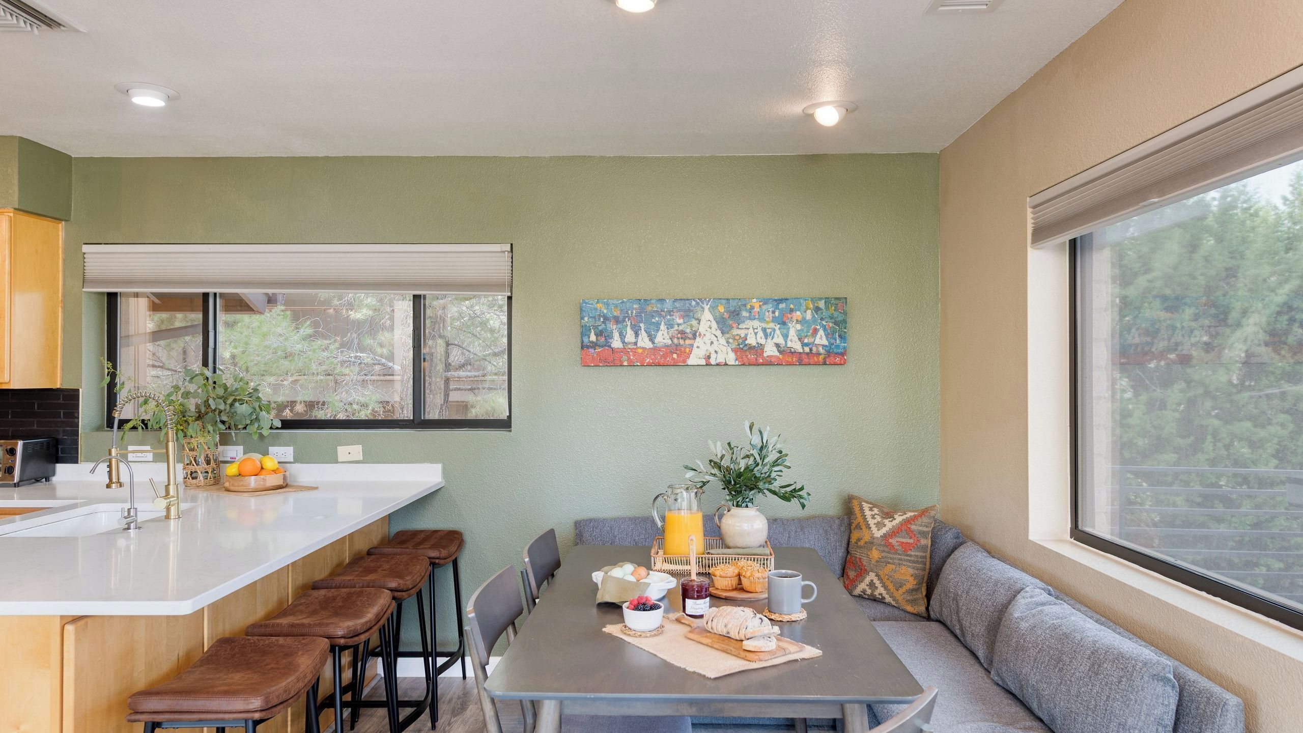 Une cuisine moderne avec un coin repas, une grande fenêtre et un tableau au mur.