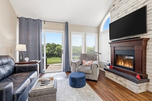 A living room with a fireplace, a sofa, a chair, a coffee table, and a view of the outdoors.
