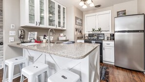 A modern kitchen with white cabinets, a granite countertop, a stainless steel refrigerator, and bar stools.