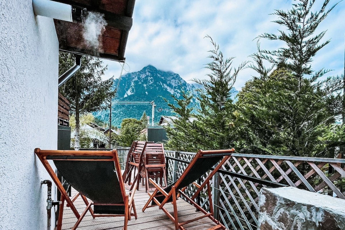 A wooden deck with chairs and a table, overlooking a mountain and trees.