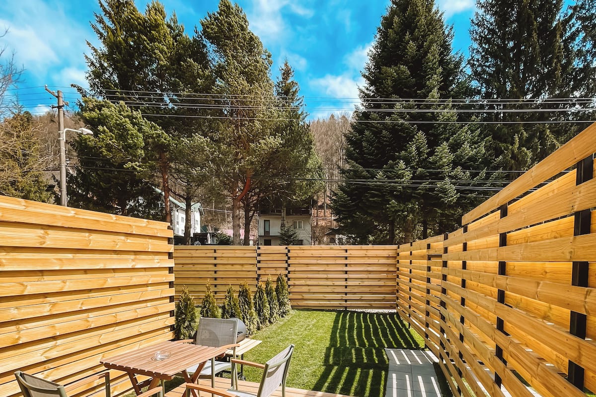 A wooden deck with a table and chairs, surrounded by a wooden fence and trees.