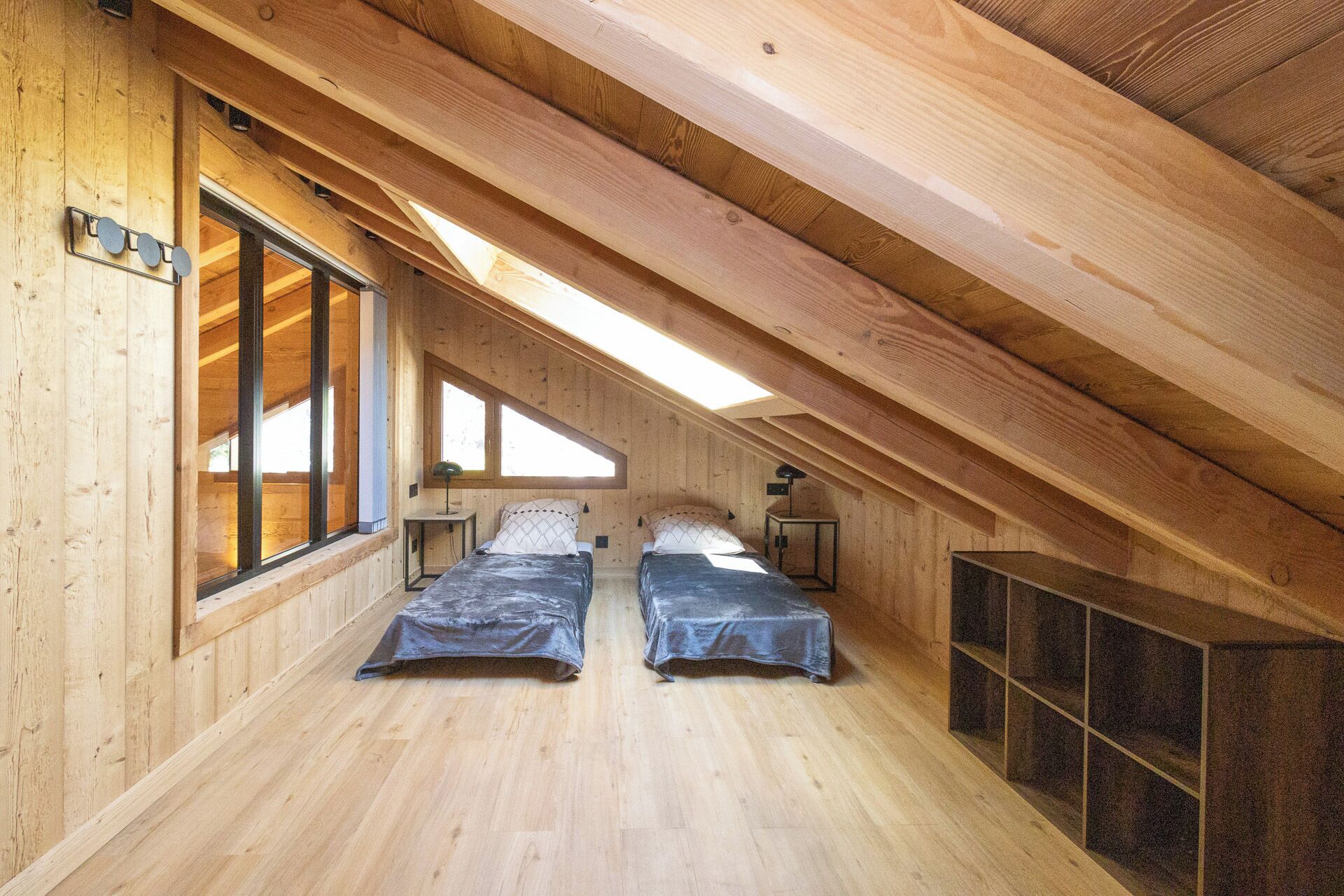Un dormitorio estilo ático acogedor con dos camas, paredes de madera y un tragaluz.