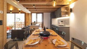 A wooden dining table with plates, glasses, and a bottle, surrounded by chairs in a room with wooden beams and a hanging light fixture. - Chalet at the foot of the slopes, private parking, free shuttle bus stop 50m away. (Les Deux Alpes)