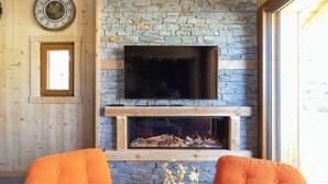 A cozy living room with a stone fireplace, a mounted television, and wooden furniture. - Chalet at the foot of the slopes, private parking, free shuttle bus stop 50m away. (Les Deux Alpes)