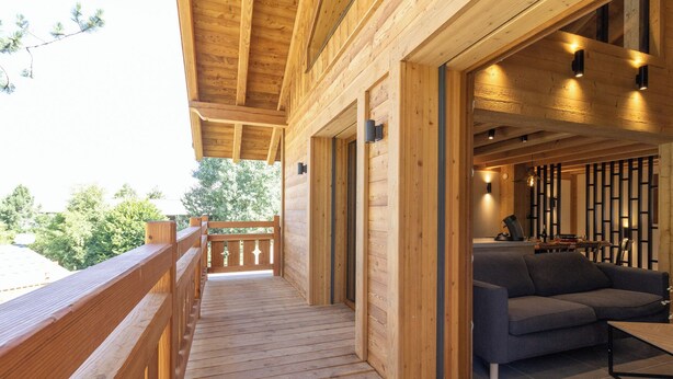 A wooden deck with a railing, a sofa, and a dining area with a table and chairs. - Chalet at the foot of the slopes, private parking, free shuttle bus stop 50m away. (Les Deux Alpes)