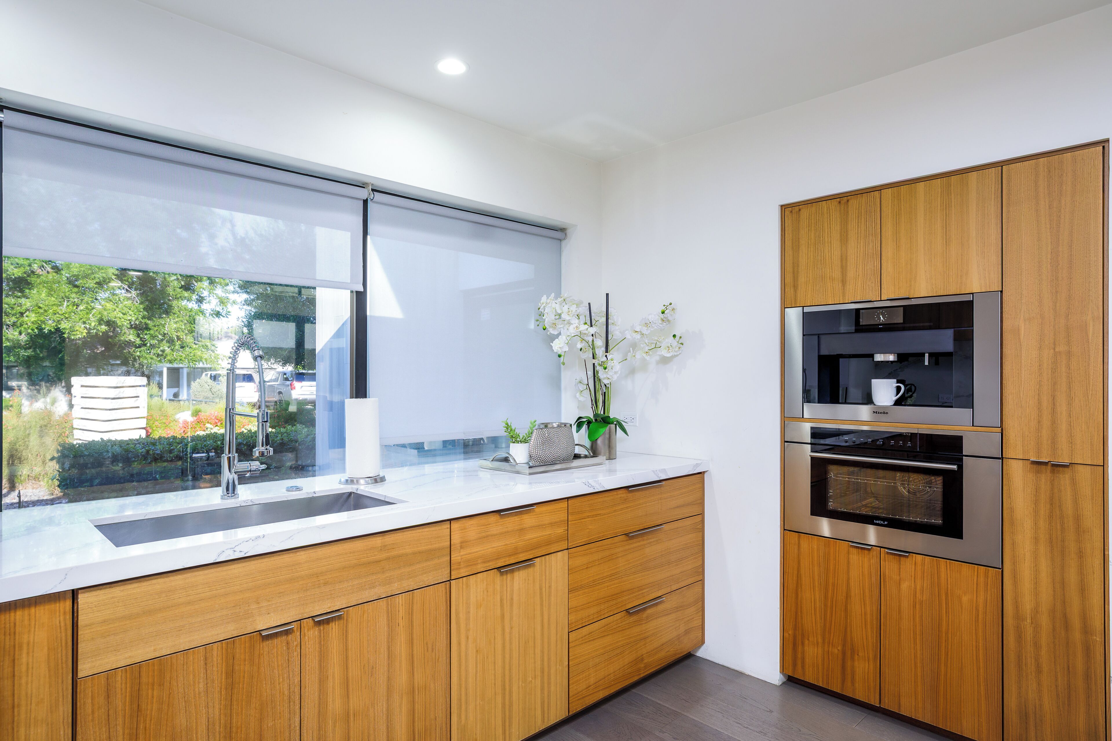 Eine moderne Küche mit Holzschränken, einem Edelstahlbackofen und einem Fenster mit Blick auf Grünflächen.