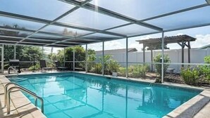A covered outdoor swimming pool with a metal frame and glass panels, surrounded by lounge chairs and potted plants. - Cape Coral Florida Getaway (Cape Coral)