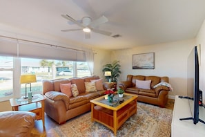 A living room with two leather sofas, a wooden coffee table, a ceiling fan, a TV, and a large window with blinds.