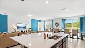 A modern kitchen with a central island, a dining area with a table and chairs, a living room with a sofa and TV, and a large window with curtains. - LAKEVIEW from Your Private Pool! Relax & Create Memories! Resort Near Disney! (Kissimmee)