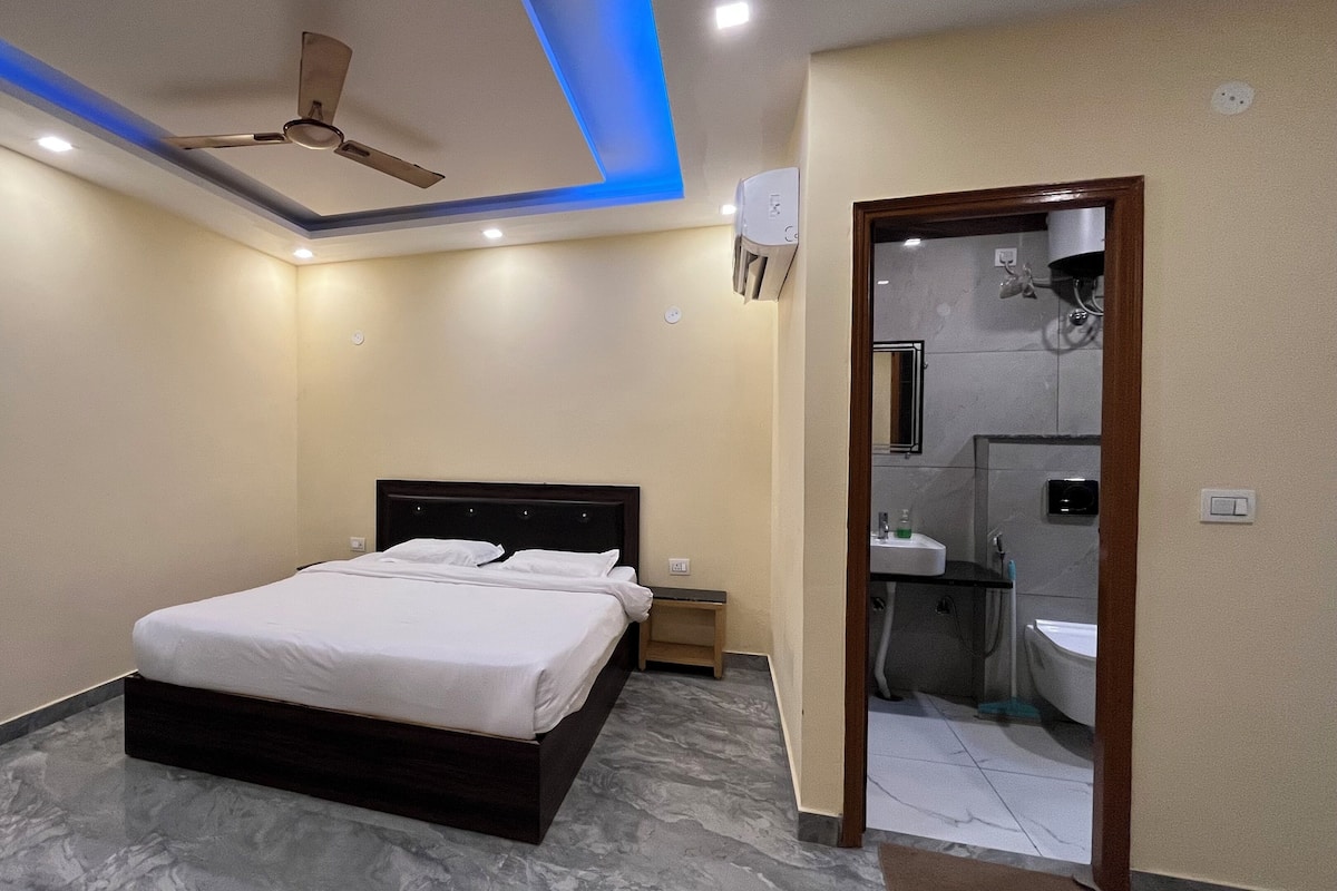 A modern bedroom with a bed, a ceiling fan, recessed lighting, and a bathroom visible through an open door.