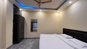 A hotel room with a bed, a ceiling fan, recessed lighting, and a dark wardrobe. - Kedar inn (Rishikesh)