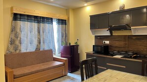 A compact kitchen with a built-in microwave, stove, and dark cabinets. A wooden bench and a small refrigerator are also visible. - Kedar inn (Rishikesh)
