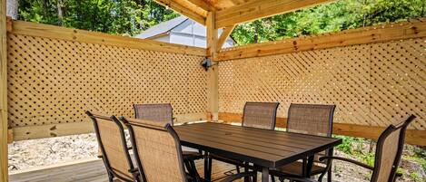 A covered outdoor patio with a wooden table and chairs, surrounded by a wooden fence with a lattice design.