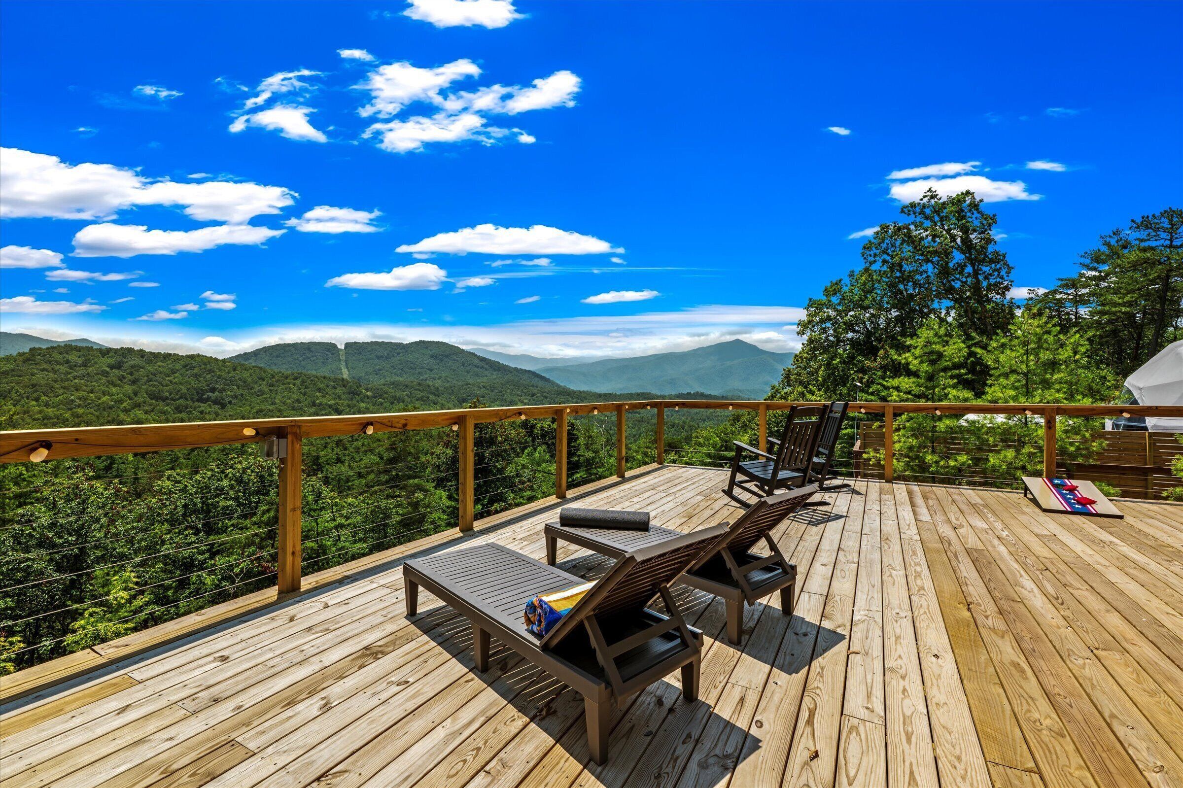 Una terraza de madera con sillones de descanso y una mesa, con vistas a un paisaje montañoso.
