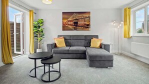 A modern living room with a grey sectional sofa, a small round table, and a cityscape painting on the wall.