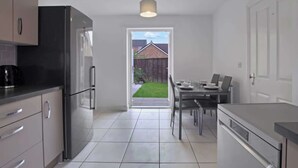 A modern kitchen with a dining area, a refrigerator, a coffee machine, and a view of a backyard.