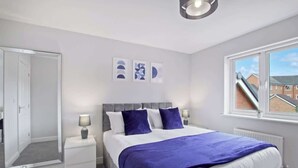 A bedroom with a bed, bedside tables, a mirror, and a window with a view of buildings.