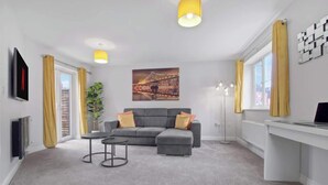 A modern living room with a grey sofa, a small round table, and a painting of a bridge.