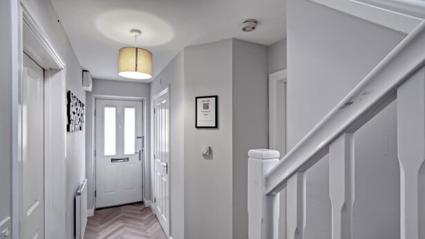 A hallway with a wooden floor, white walls, a door, a framed picture, and a staircase.