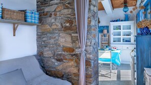 A cozy room with a stone wall, a grey sofa, a dining table with a blue tablecloth, and a white cabinet with glass doors. - Casetta Ricci - Les Azedarachs II (Brando)