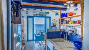 A compact kitchen with a view of the sea, a dining area with a table and chairs, and a sink with hanging utensils. - Casetta Ricci - Les Azedarachs II (Brando)