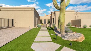 A well-maintained outdoor area with a stone pathway leading to a building entrance, surrounded by greenery and a large cactus. - Catalina Dreamin' Luxe Foothills Oasis w/Pool! (Tucson)