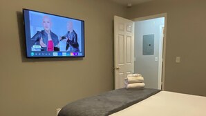 Une chambre d’hôtel avec un lit, un téléviseur fixé au mur, un ventilateur de plafond et une porte donnant sur une autre pièce.