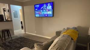 Un salon avec un canapé gris, un téléviseur à écran plat fixé au mur et un tapis gris foncé.