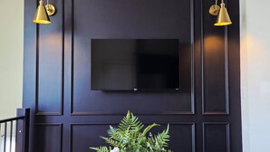 Una pared con marco negro con un televisor de pantalla plana centrado sobre un florero blanco con follaje verde y un objeto decorativo.
