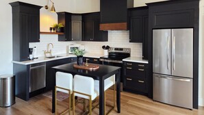 Una cocina moderna con armarios oscuros, electrodomésticos de acero inoxidable y una isla central con sillas.