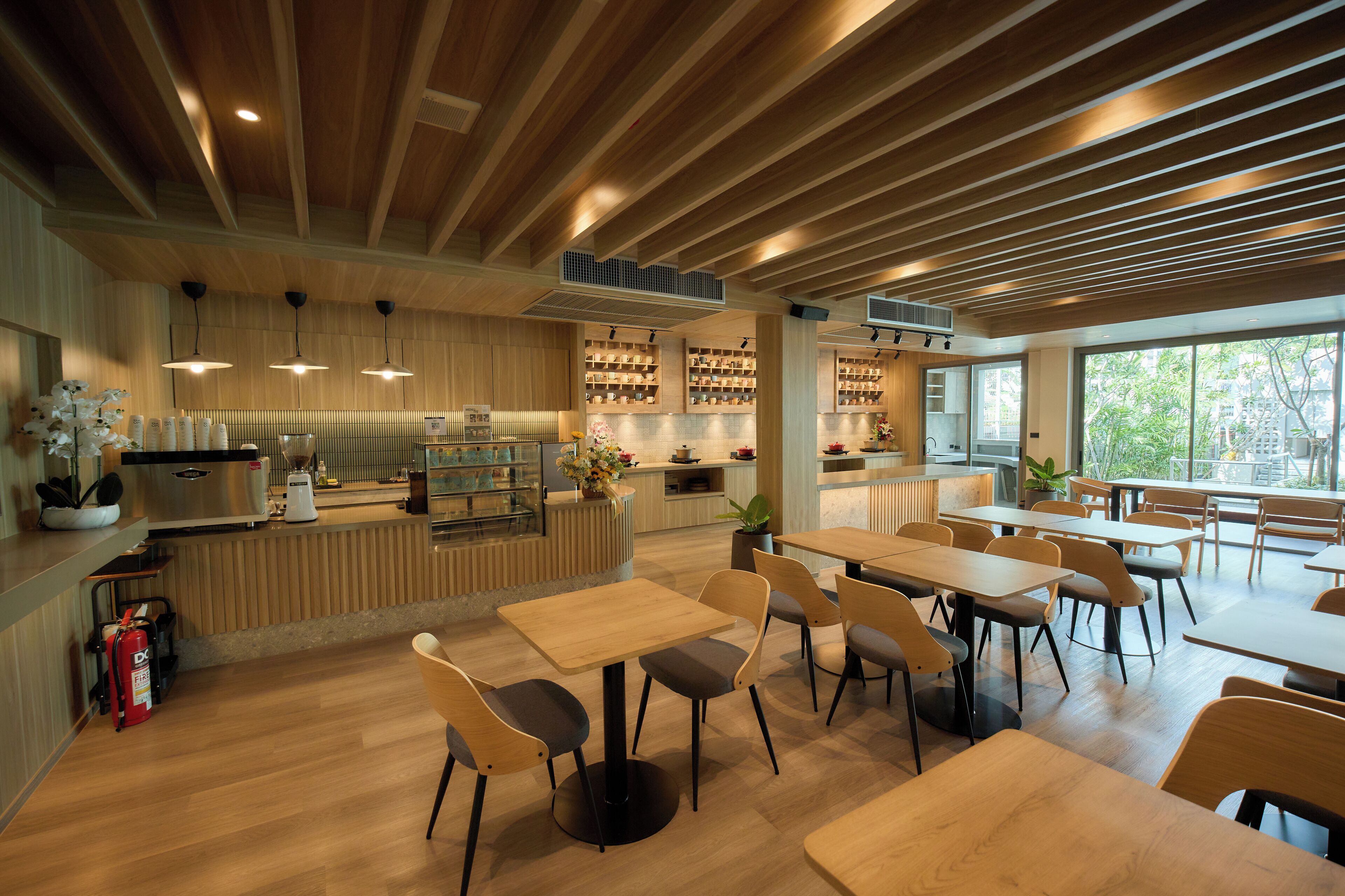 A modern cafe with wooden ceiling beams, a counter with a display of items, and tables and chairs arranged for seating.