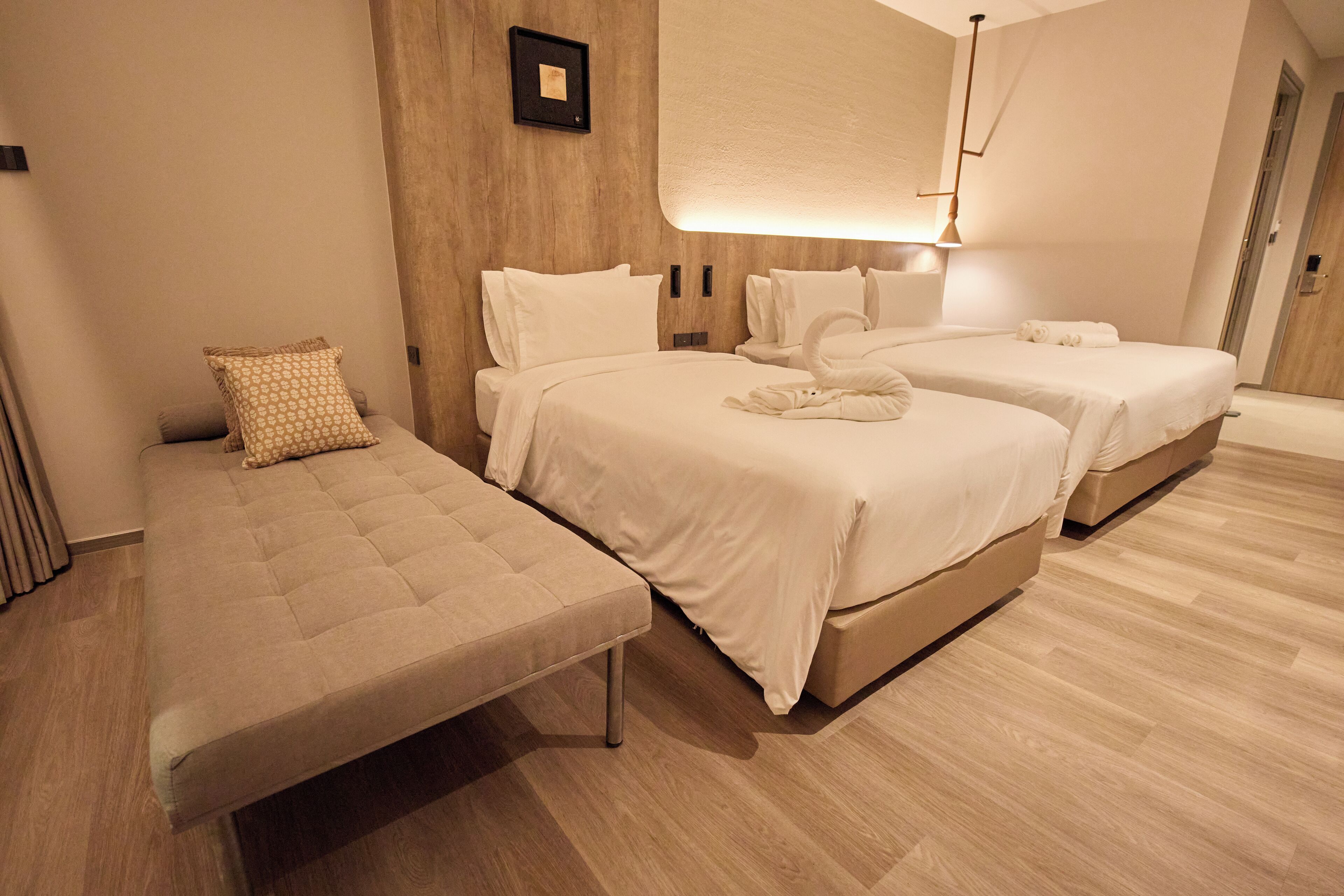 A hotel room with two beds, a sofa, and a wooden floor.