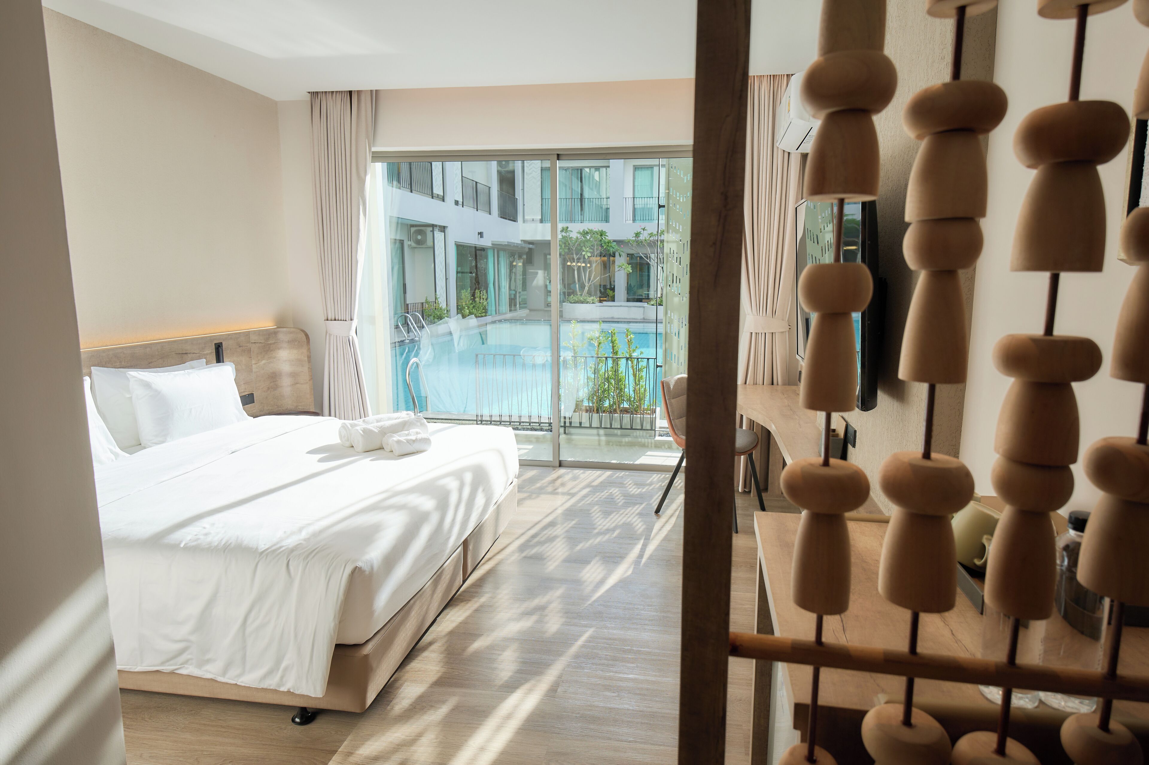 A hotel room with a bed, a desk, and a view of a pool and building.