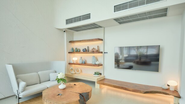 Un salon moderne avec un canapé blanc, une table basse en bois, un banc en bois et une étagère ornée d’objets décoratifs.
