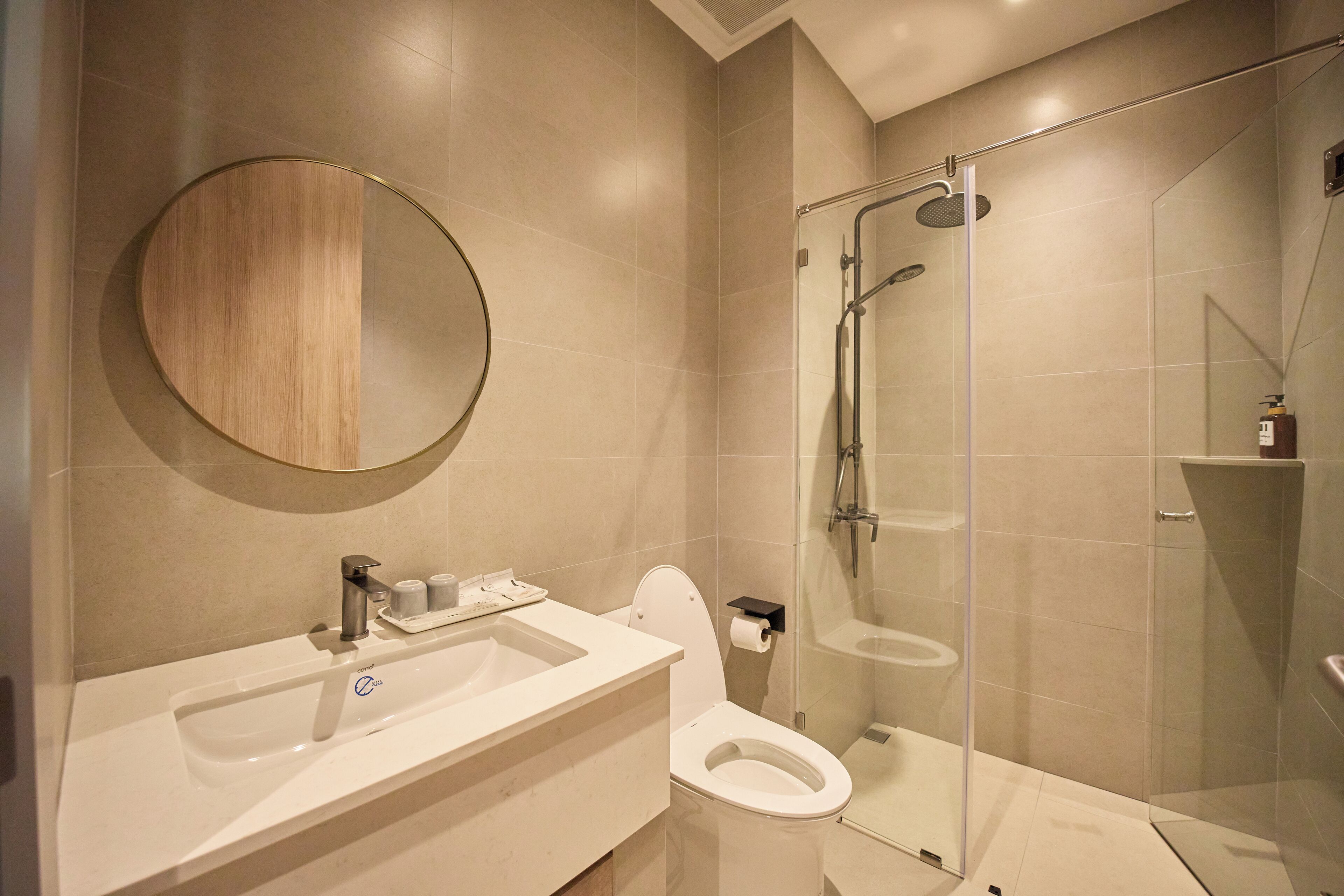 A modern bathroom with a glass-enclosed shower, a round mirror, and a white sink.