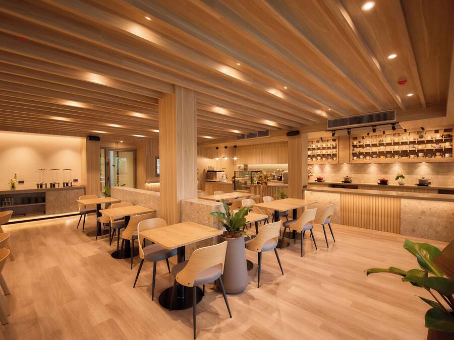 A modern restaurant interior with wooden flooring, tables, chairs, and a bar area.
