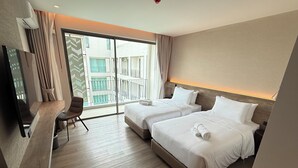 Une chambre d’hôtel avec deux lits, un bureau et une chaise. Une grande fenêtre offre une vue sur les bâtiments environnants.