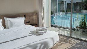 Une chambre d’hôtel avec un grand lit, du linge de lit blanc, une vue sur une piscine et un balcon agrémenté de plantes en pot.