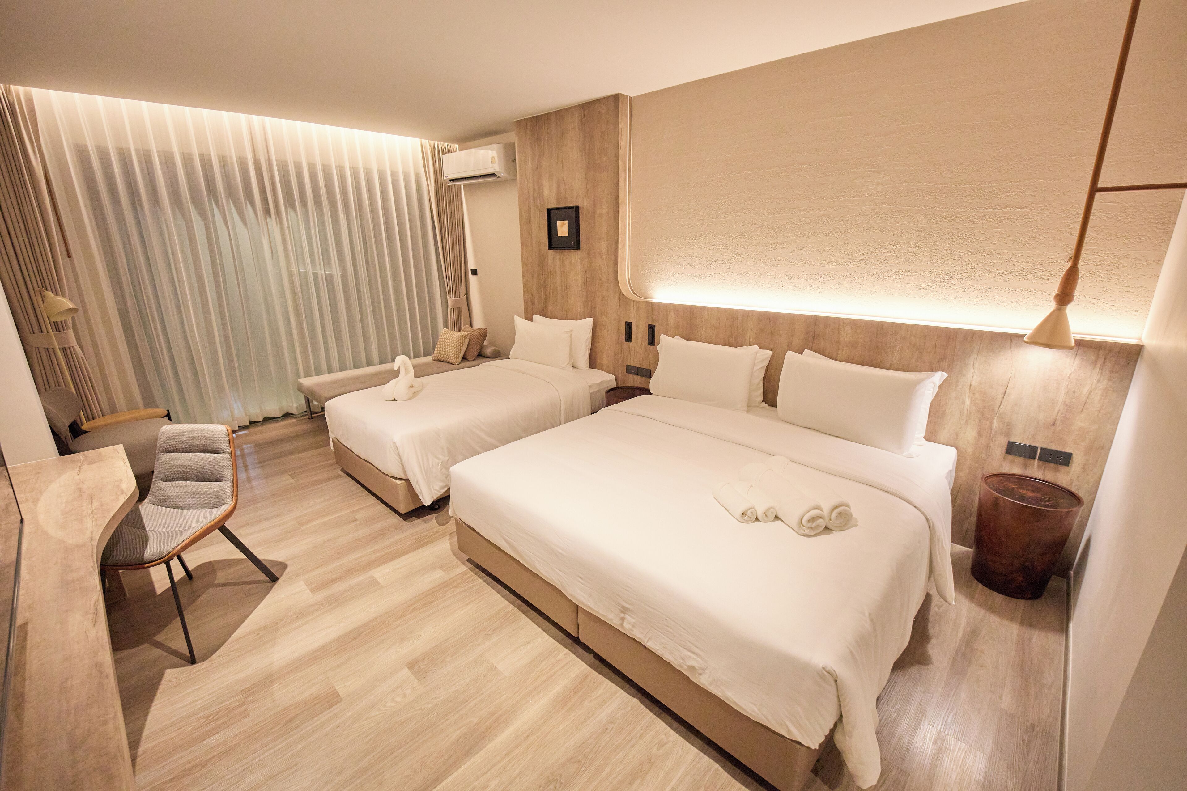 Ein modernes Hotelzimmer mit zwei Betten, einem Schreibtisch und einem Sessel.