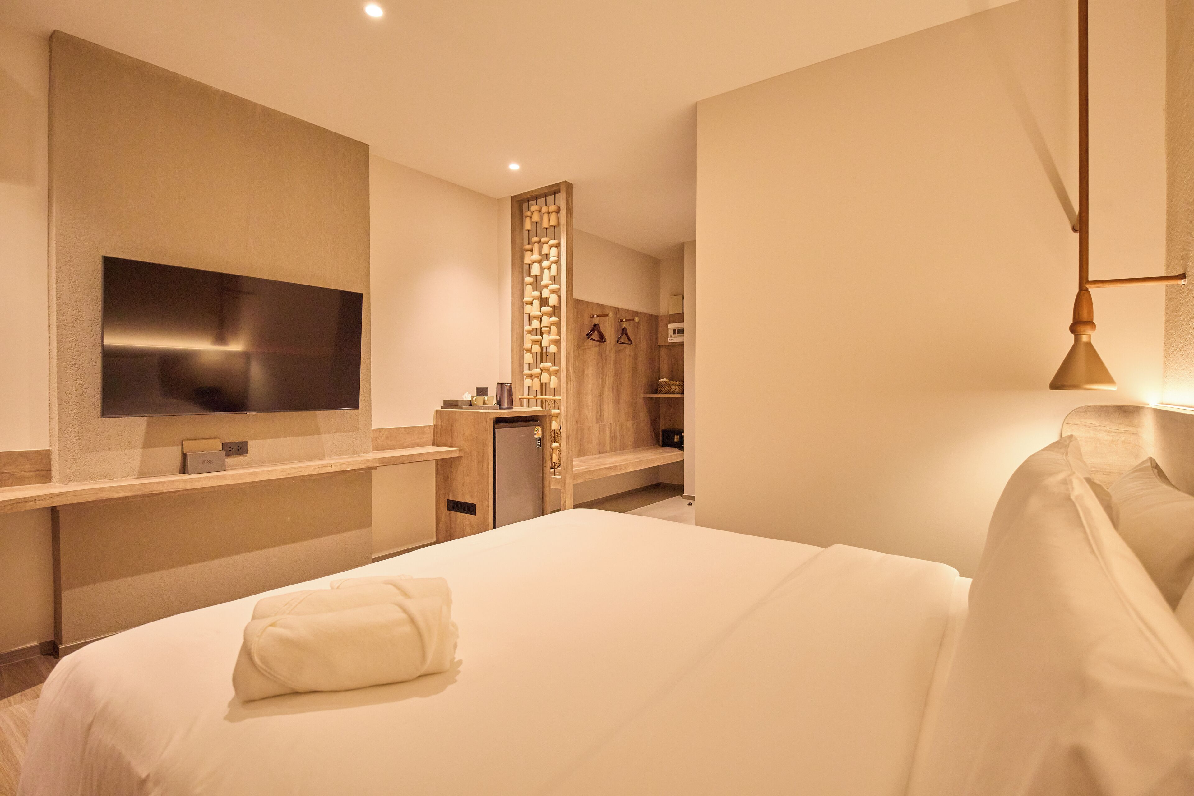 A modern hotel room with a large bed, a flat-screen TV mounted on the wall, a wooden cabinet, and a small desk.