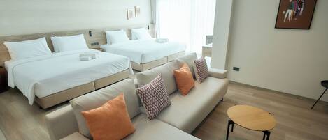 A modern hotel room with two beds, a sofa, and a small table.