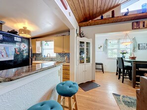 A kitchen with a refrigerator, a sink, and cabinets. There is a dining area with a table and chairs. - Crescent Beach Cottage | Dog-Friendly (St. Augustine)