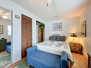 A bedroom with a bed, bedside table, lamp, and a blue armchair. - Crescent Beach Cottage | Dog-Friendly (St. Augustine)